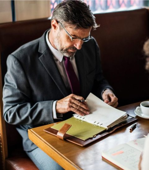 A man in a suit and tie sitting at a table with a notebook.